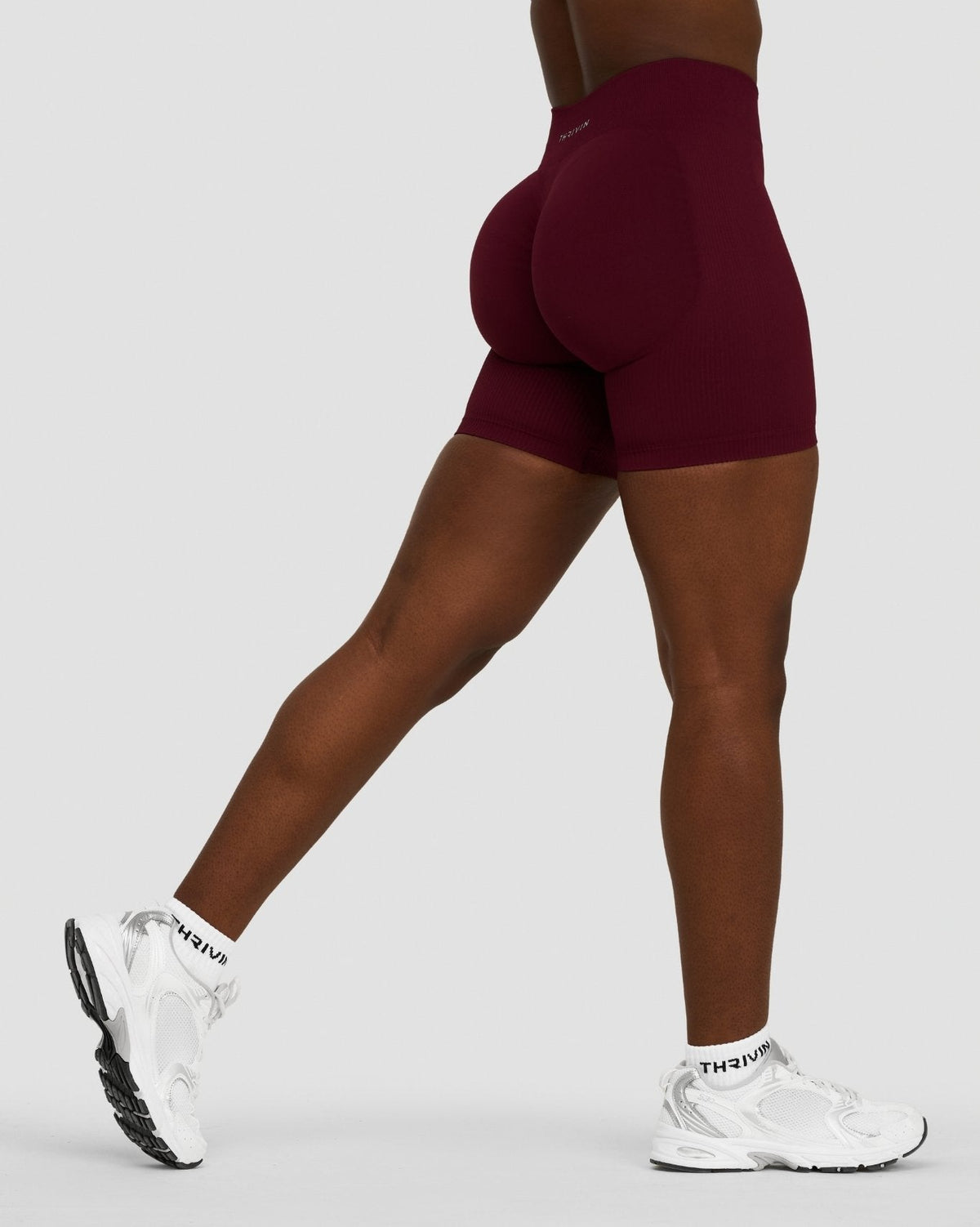 Elevate Sculpting Mid Waist Scrunch Shorts in Merlot, side view mid-stride with white sneakers