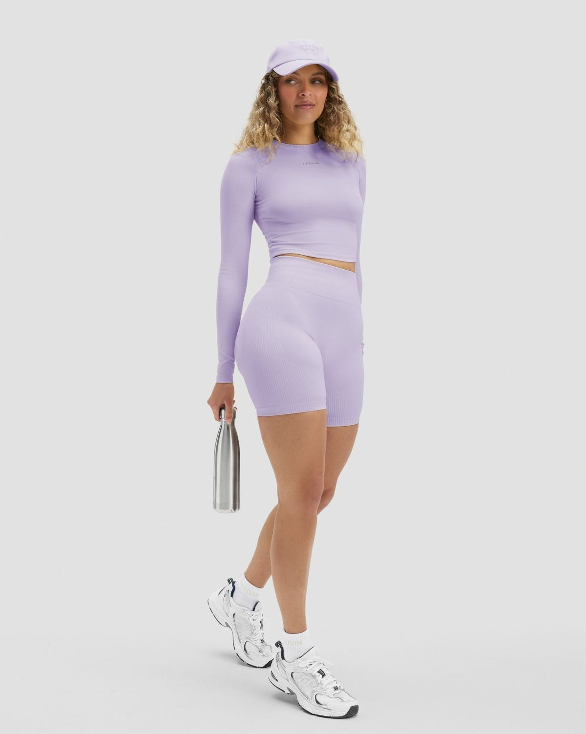 Elevate Sculpting High Waist Scrunch Shorts in Lilac, full-length front view holding a water bottle