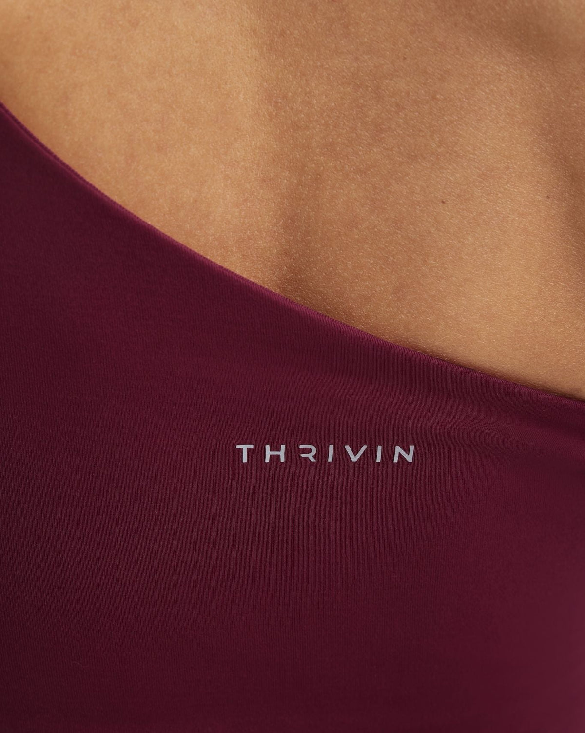 Elevate Sculpting Asymmetric Twist Top in Cherry Berry, close-up of shoulder strap and THRIVIN logo