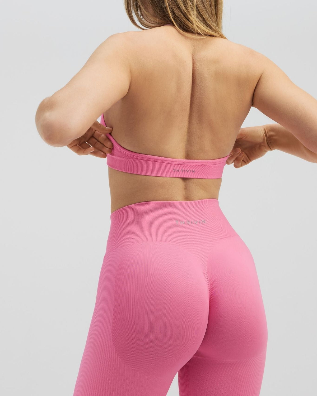 Elevate Sculpting Seamless Adjustable Halter Bra in Bubble Pink, back view with hands at straps, styled with leggings