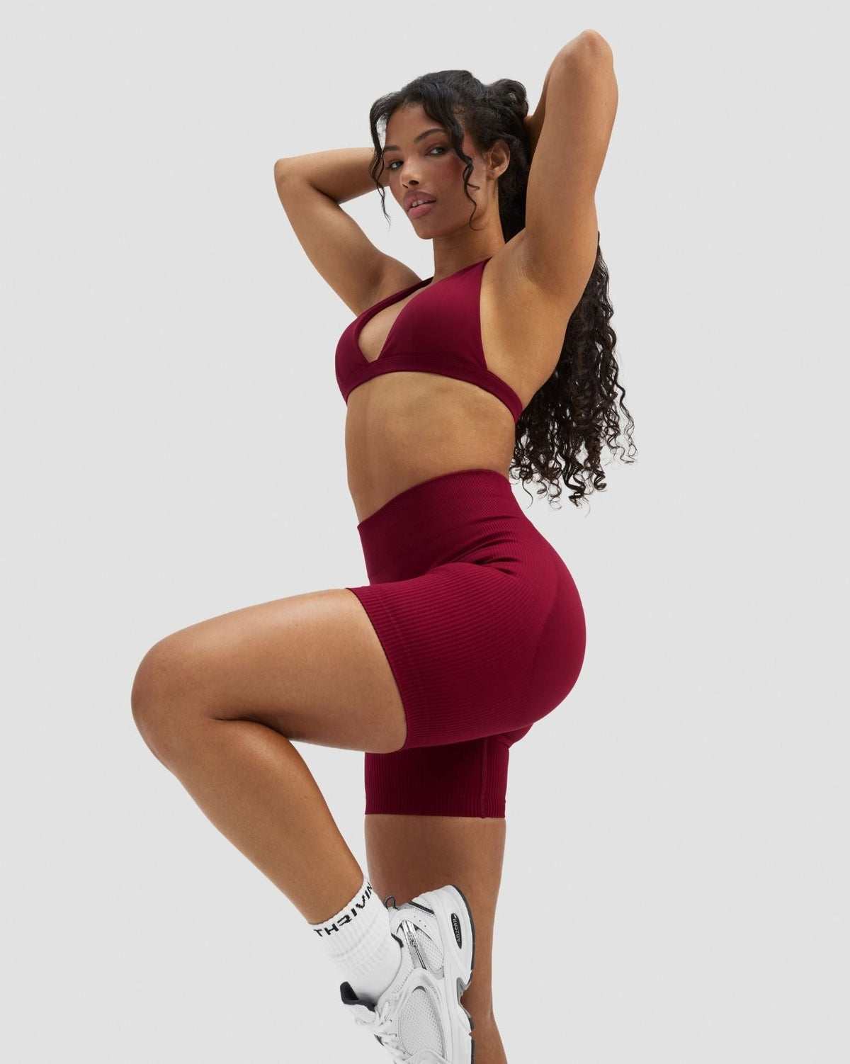 Elevate Sculpting Mid Waist Scrunch Shorts in Raspberry, front view with arms raised, styled with matching bra