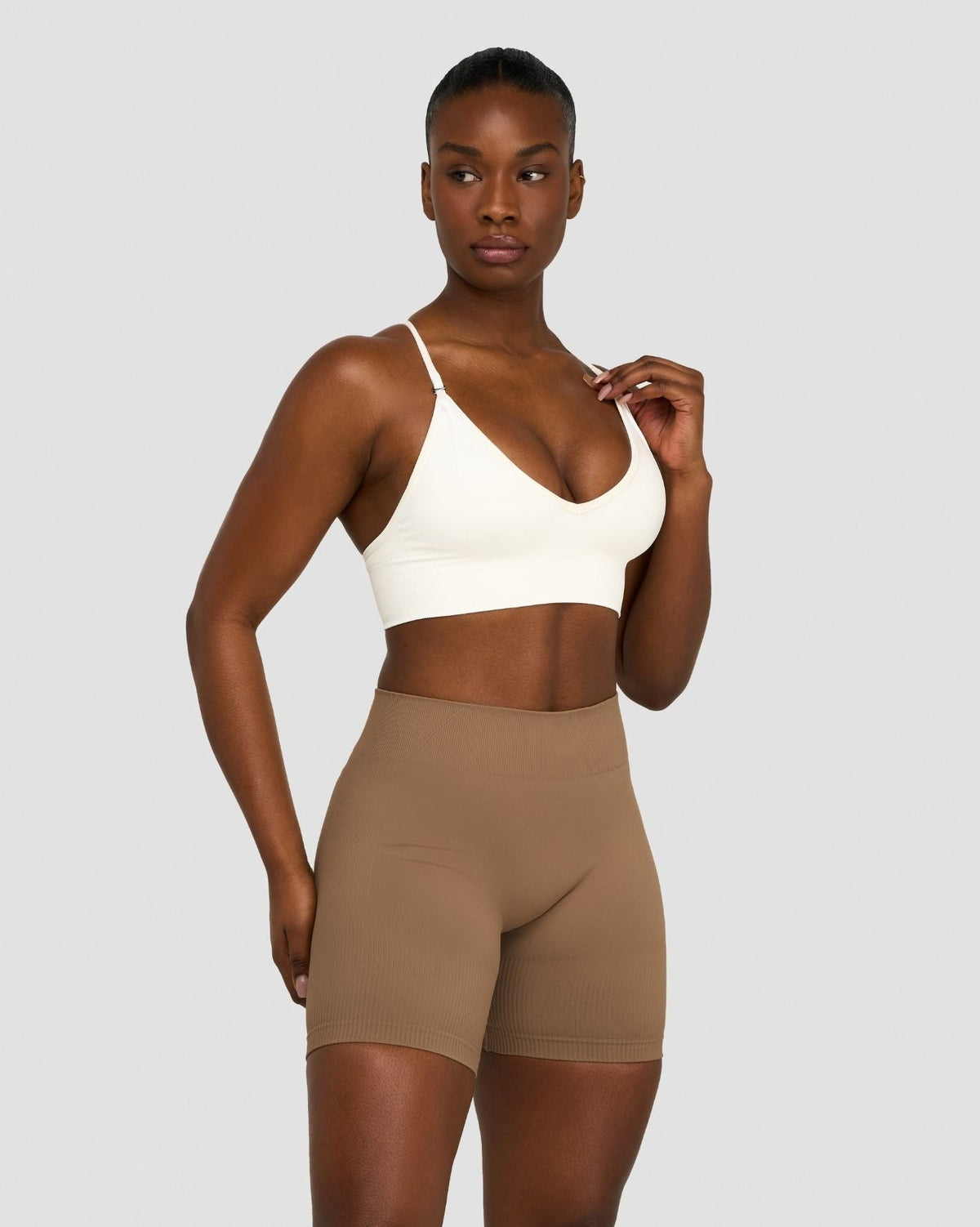 Elevate Multiway Sculpt Seamless Bra in Cream, front view, hand at strap, styled with shorts