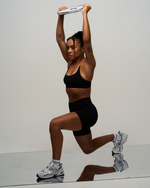 Elevate Sculpting Seamless Scoop Neck Bra in Night Black, front view in a lunge with arms raised, styled with black shorts
