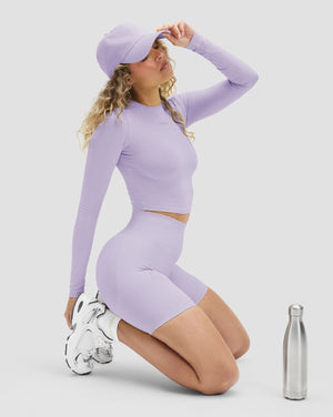 Elevate Sculpting High Waist Scrunch Shorts in Lilac, kneeling beside a water bottle, styled with a long sleeve top
