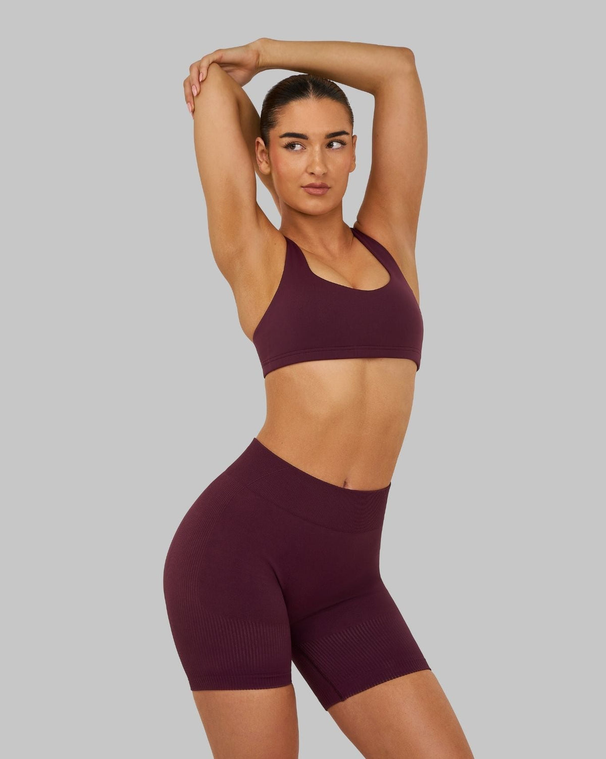 Elevate Sculpting Medium Impact Multiway Bra in Winter Plum Red, front view with arm raised, styled with shorts