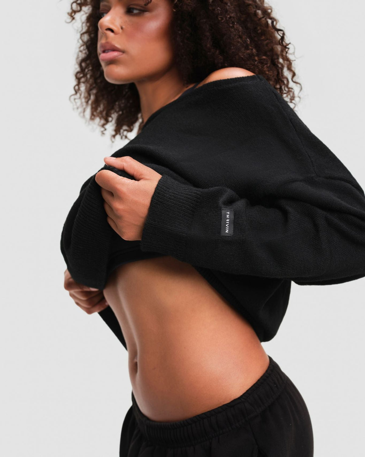 The Essential Collection Off The Shoulder Wool Blend Sweater in Night Black, side close-up of THRIVIN logo tab on the cuff